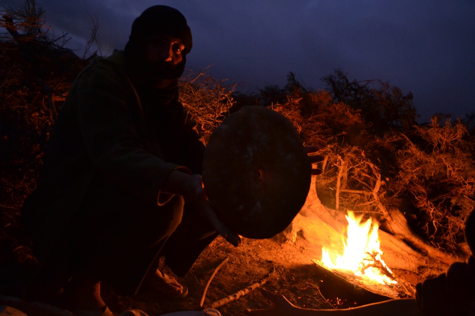 Amazigh nomad in southern Morocco baking bread in an underground oven. The dough is put in a round container submerged in the sand, then a lid is placed on top. This man used an old oil drum. Imazighen pile tinder on the lid, and burn it to bake the bread below. This process is usually the domain of women in Amazigh society. However, none of the women of this family wanted to be photographed, so this man volunteered himself for the shot. Apparently, his bread wasn't quite as good as his daughter's.